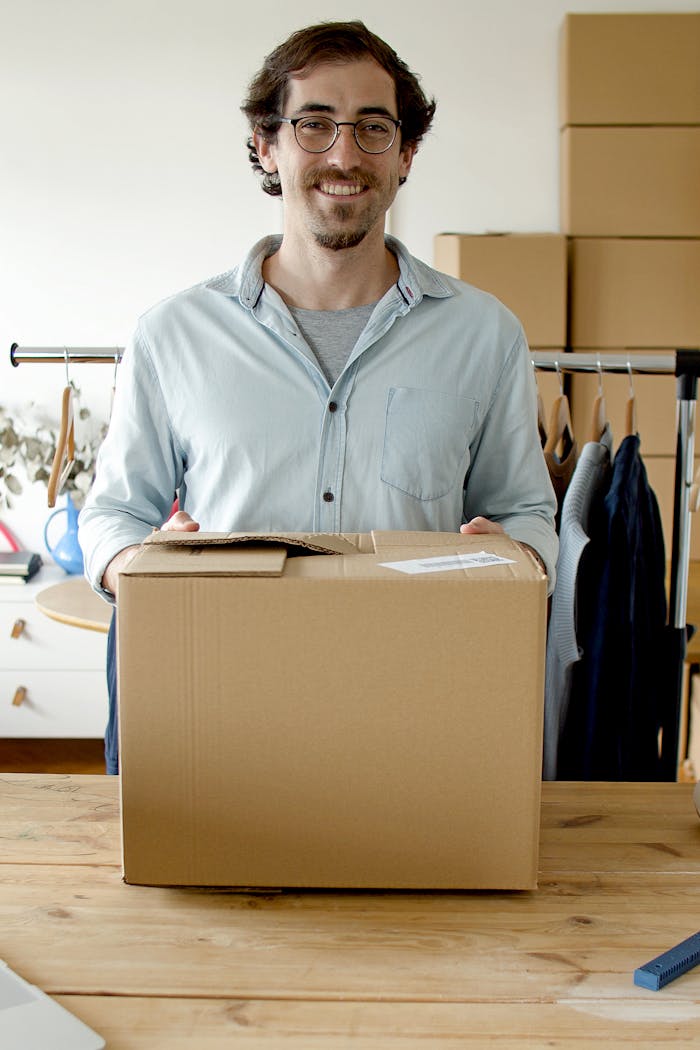 A cheerful businessman holding a package in a modern indoor workspace, signifying small business and entrepreneurship.